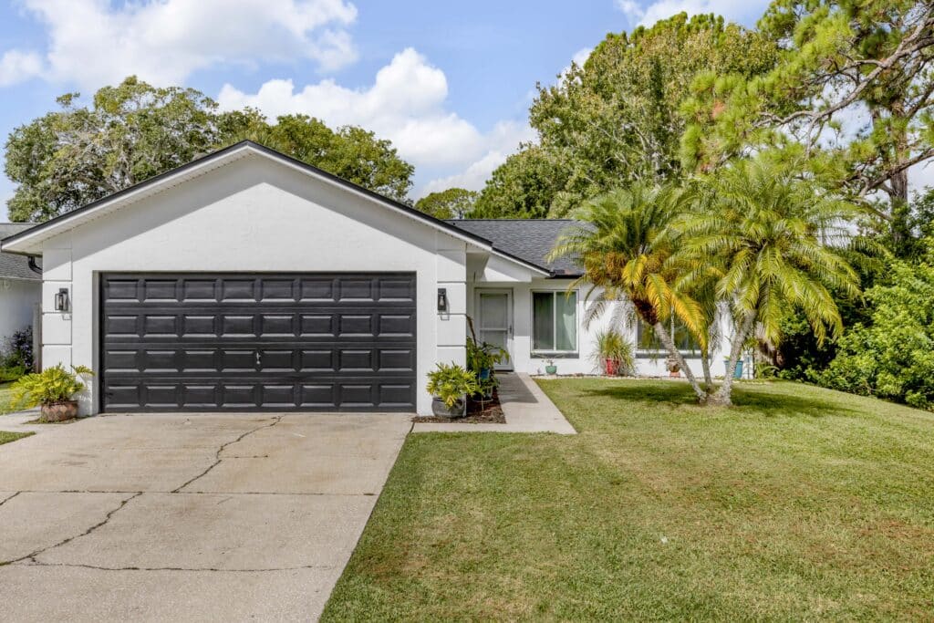 White stucco house with black garage door and palm trees, ideal for local living real estate.
