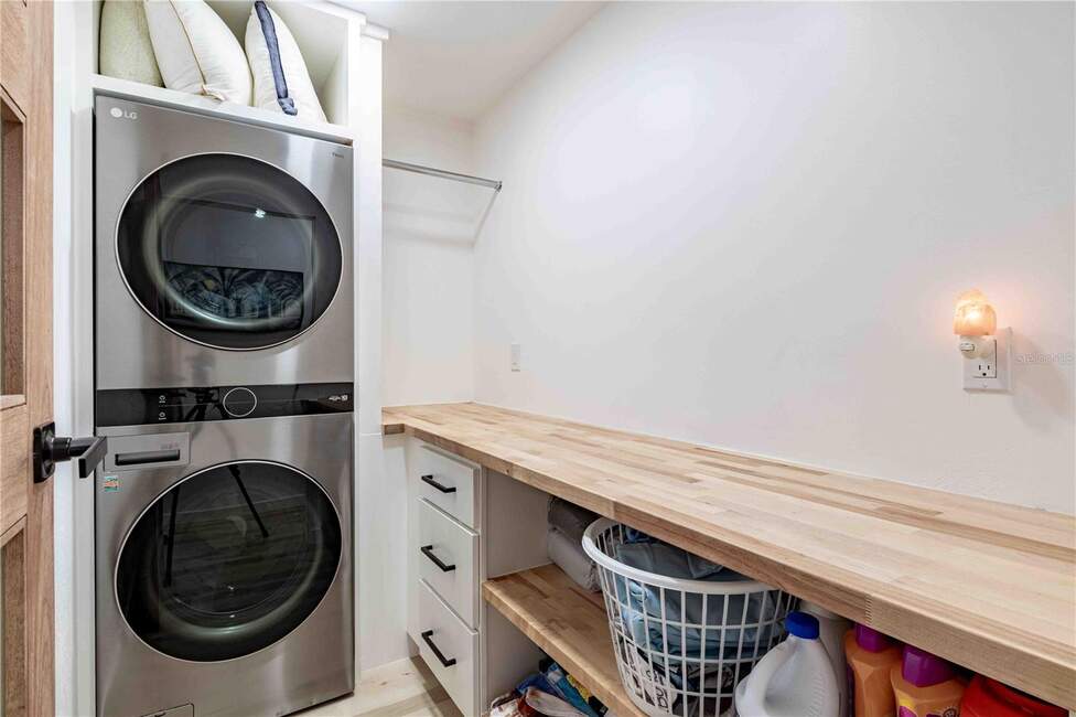 Modern laundry room with stacked LG washer/dryer and butcher block countertop.