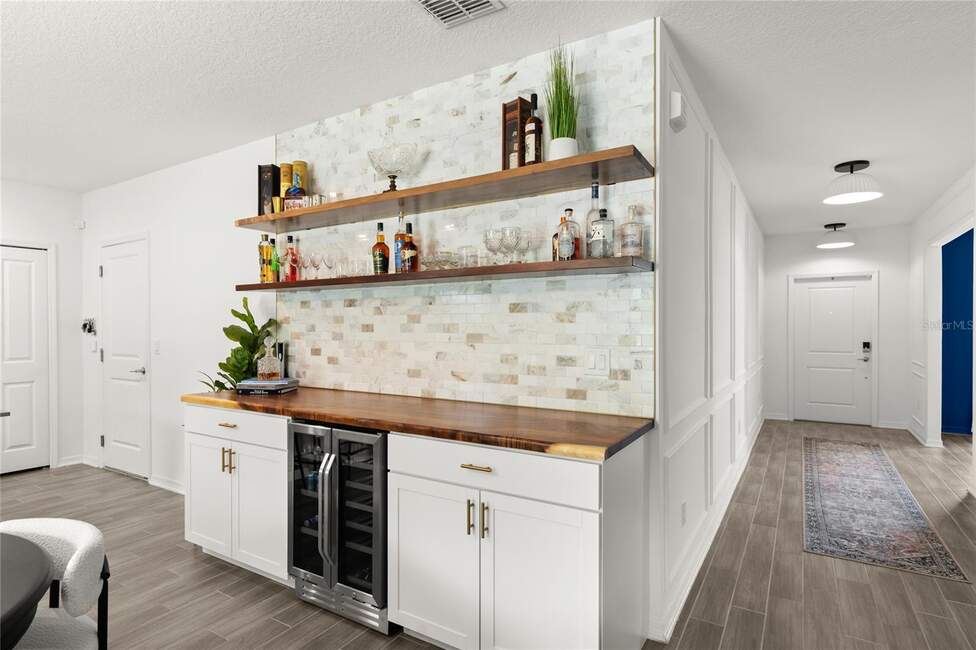 Built-in home bar with wine fridge, liquor bottles, and marble tile backsplash.