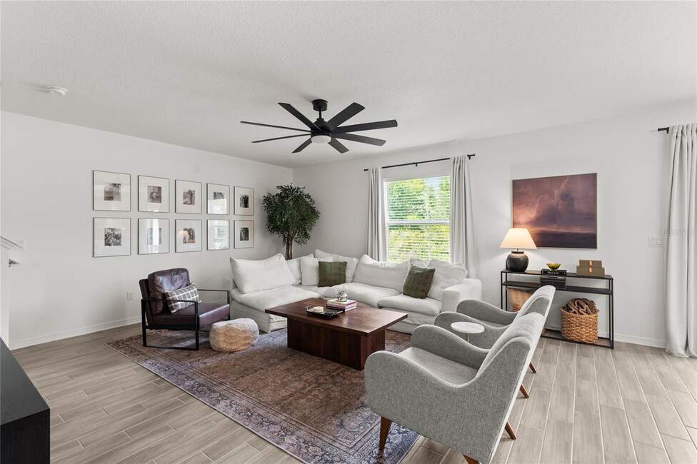 Living room at 2516 Hoptree Ln, Edgewater, FL: white sectional, rug, chairs, artwork.